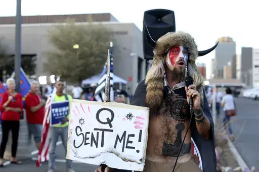 Jacob Anthony Chansley, who also goes by the name Jake Angeli, a Qanon believer speaks to a crowd of President Donald Trump supporters outside of the Maricopa County Recorder's Office where votes in the general election are being counted, in Phoenix on Nov. 5, 2020. From the Salem witch trials to fears of the Illuminati to the Red Scare to QAnon, conspiracy theories have always served as dark counter programming to the American story taught in history books. (AP Photo/Dario Lopez-Mills, File)