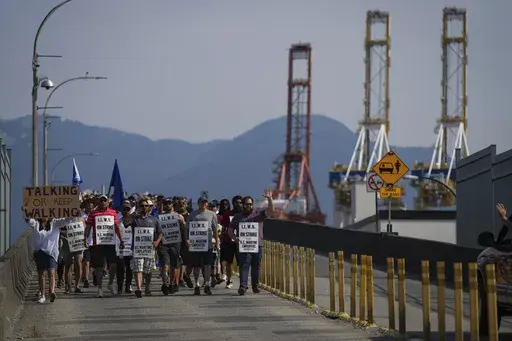 Striking International Longshore and Warehouse Union Canada workers march to a rally as gantry cranes used to load and unload cargo containers from ships sit idle at port, in Vancouver, on Thursday, July 6, 2023. (Darryl Dyck /The Canadian Press via AP)