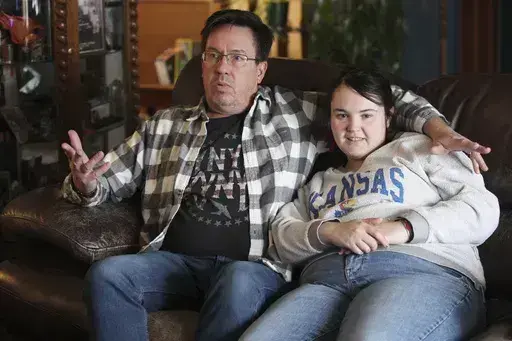 Rick Elskamp sits with his oldest daughter, Sheridan, and discusses the frustrations of having his 23-year-old daughter on a waiting list for 10 years for services as an intellectually disabled adult, Saturday, Jan. 27, 2024, at the Elskamps' home outside Topeka, Kan. Thousands of Kansas residents with disabilities and hundreds of thousands across the U.S. are on waiting lists for services. (AP Photo/John Hanna)