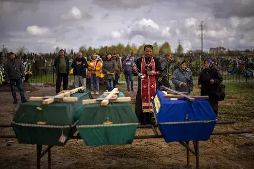 A priest blesses the remains of three people who died during the Russian occupation and were disinterred from temporary burial sites in Bucha, on the outskirts of Kyiv, on Wednesday, April 27, 2022. (AP Photo/Emilio Morenatti)