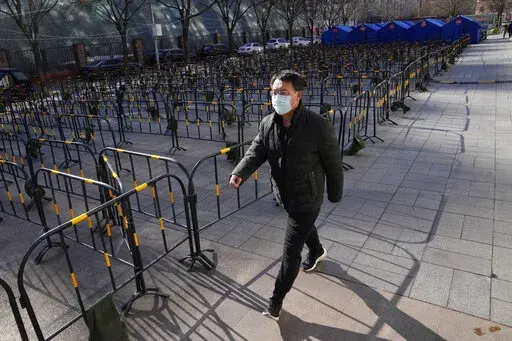 A resident wearing a mask to help protect from the coronavirus walks past barricades and tents prepared for mass testing at a neighborhood in Beijing, China, Saturday, Jan. 29, 2022. Chinese are traveling to their hometowns for the Lunar New Year, the country's biggest family holiday, despite a government plea to stay where they are as Beijing tries to contain coronavirus outbreaks. (AP Photo/Ng Han Guan)