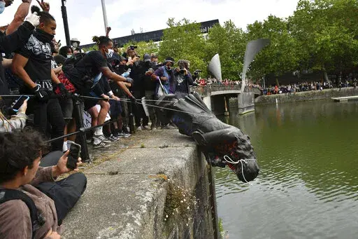 Protesters throw a statue of Edward Colston into the Bristol harbour during a Black Lives Matter protest rally, Bristol, England, June 7, 2020. Four anti-racism demonstrators were cleared Wednesday Jan. 5, 2022, of criminal damage in the toppling of a statue of a 17th century slave trader during a Black Lives Matter protest in southwestern England 18 months ago. (Ben Birchall/PA via AP, File)