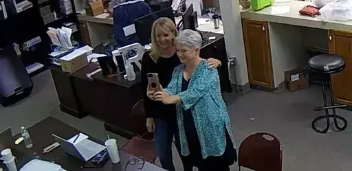 In this Jan. 7, 2021, image taken from Coffee County, Ga., security video, Cathy Latham, right, appears to take a selfie with a member of a computer forensics team inside the local elections office. Lawyers for three Georgia Republicans, including Latham, who falsely claimed that Donald Trump won the state and they were “duly elected and qualified” electors, are set to argue that their criminal charges should be moved from state to federal court(Coffee County, Georgia via AP)