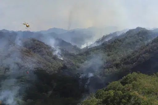 This photo provided by the Hawaii Department of Land and Natural Resources shows an Army helicopter carrying water to douse a wildfire burning east of Mililani, Hawaii, on Thursday, Nov. 2, 2023. A wildfire that has burned forestlands in a remote mountainous area of Central Oahu has moved eastward and away from population centers as firefighters continued to battle the blaze. (Dan Dennison/Hawaii Department of Land and Natural Resources via AP)