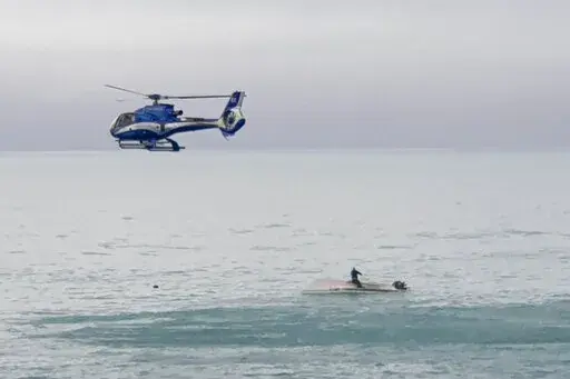 A helicopter flies overs an upturned boat with a survivor sitting on the hull off the coast of Kaikoura, New Zealand, Saturday, Sept. 10, 2022. A boat in New Zealand collided with a whale and capsized. (AP Photo)