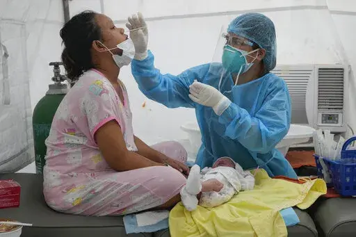 Medical Technologist Erika Alvarado performs a COVID-19 test on a patient who just delivered a baby outside a hospital in Manila, Philippines on Friday, Dec. 24, 2021. In the Philippines, one of the worst-hit by the pandemic in Southeast Asia, daily COVID-19 infections have considerably dropped from an average 22,000 cases just three months ago during an alarming spike set off by the delta variant to just a few hundred in recent days after a delayed vaccination campaign considerably intensified 