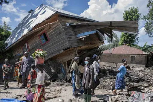 People walk next to a house destroyed by the floods in the village of Nyamukubi, South Kivu province, in Congo, Saturday, May 6, 2023. The death toll from flash floods and landslides in eastern Congo has risen according to the governor and authorities in the country's South Kivu province. (AP Photo/Moses Sawasawa)