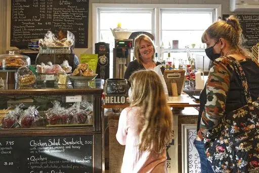 Cafe owner Maureen Donnelly Morris talks to customers at Back Street Brews, on Dec. 16, 2021, in Lovettsville, Va., a gathering spot where neighbors of all political persuasions come together for coffee and civil chat. In the neighborhood, the mix of pro-Trump signs, gay-pride rainbow flags and Black Lives Matter banners speaks to a striking diversity in political views and an undercurrent of tension that plays out unfiltered on Facebook. But in this "coffee bubble," left, right, red and blue ge