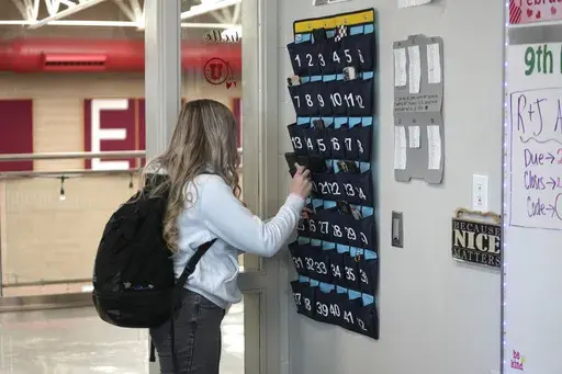 A ninth grader places her cellphone in to a phone holder as she enters class at Delta High School, Friday, Feb. 23, 2024, in Delta, Utah. Most schools have policies regulating student cellphone use at school. But the reality is kids don’t always follow the rules and schools enforce them sporadically. (AP Photo/Rick Bowmer, File)