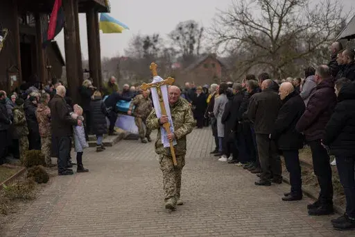 People attend a funeral ceremony for Ukrainian military servicemen Roman Rak and Mykola Mykytiuk in Starychi, western Ukraine, Wednesday, March 16, 2022. Rak and Mykytiu were killed during Sunday's Russian missile strike on a military training base in Yavoriv. (AP Photo/Bernat Armangue)